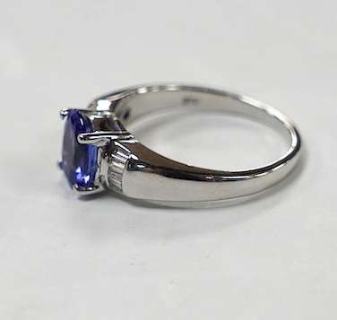 A modern 18ct gold and single stone oval cut tanzanite set ring, with baguette cut diamond cluster set shoulders, with accompanying AnchorCert report, stating the stone to weigh 1.20ct, size L, gross weight 4.1 grams. Co